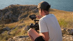 Filmmaker with camera on tripod changes settings and shoots a sea sunset.