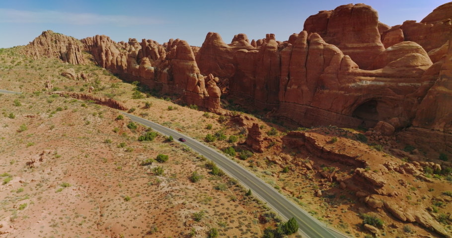 Cars moving by the motorway locating along the odd-shaped orange rocks. Wonderful canyons of Arches national park, Utah, USA.