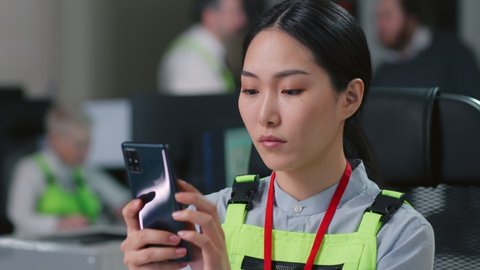 Asian woman technician using smartphone sitting at desk in industrial office. Construction worker or engineer chat on mobile phone