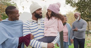 Video of happy african american parents walking in garden holding daughter with grandparents behind. Family, domestic life and togetherness concept digitally generated video.