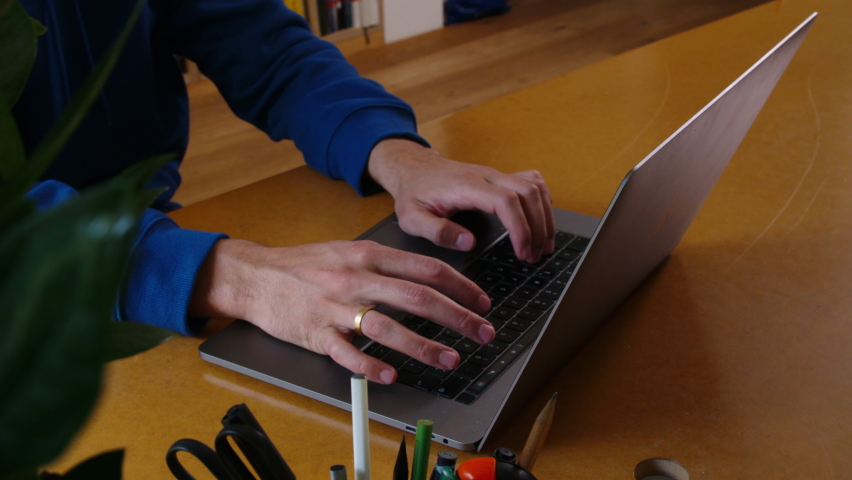 Hands of adult working on laptop keyboard at home. High angle view. 