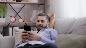 Handsome young man using smartphone and laughing. Happy smiling hipster man with top knot using mobile phone apps, texting message, browsing internet, watching video, tapping, looking at smartphone.