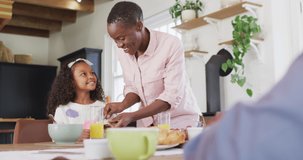 Video of happy african american mother buttering bread for daughter at family breakfast table. Family, domestic life and togetherness concept digitally generated video.