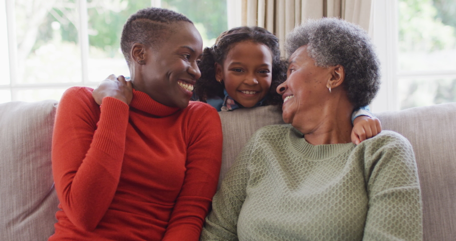 Video of smiling african american mother, daughter and grandmother sitting hugging in living room. Family, domestic life and togetherness concept digitally generated video. Royalty-Free Stock Footage #1093087863