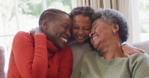 Video of smiling african american mother, daughter and grandmother sitting hugging in living room. Family, domestic life and togetherness concept digitally generated video. - Βίντεο στοκ