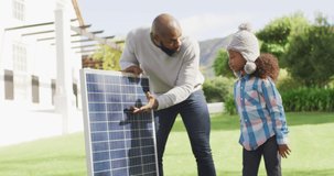 Video of happy african american father explaining solar panel to daughter in sunny garden. Family, domestic life and togetherness concept digitally generated video.