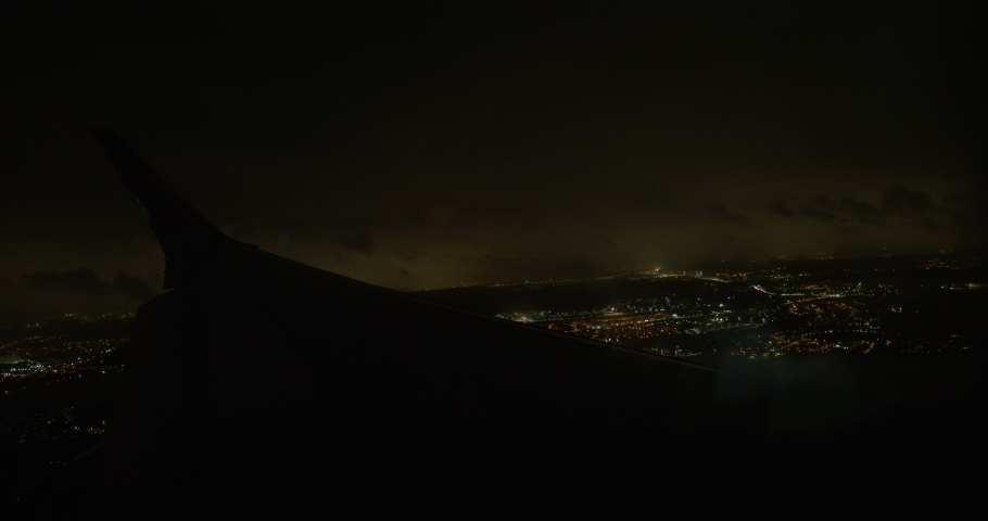 Looking from flying airplane at night. Aircraft descending over the illuminated city, blinking light on the wing. Arriving to the place of destination Royalty-Free Stock Footage #1093088139