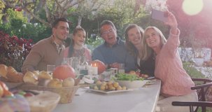 Video of happy caucasian parents, daughter and grandparents taking selfie at outdoor dinner table. Family, domestic life and togetherness concept digitally generated video.