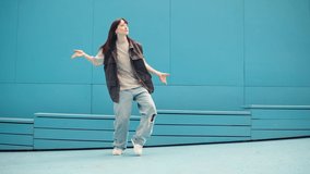 Young woman dancing hip hop on blue background wall. Modern dance choreography. Female professional street dancer showing dance movings. Musical video.