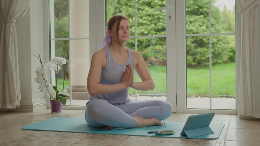 Young adult woman doing yoga exercise and meditation practice at home. Female resting with aroma sticks sitting on fitness mat on the floor. Royalty-Free Stock Footage #1093094081