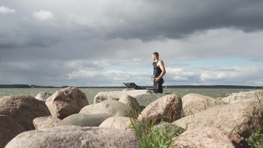 Motivation, pro racer stand near the lake, a cyclist resting after triathlon training, cloudy weather.