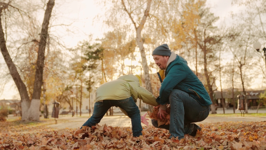 Father and little child in an autumn park throw dry leaves up, happy family, live fun with dad, cheerful kid plays with foliage and parent hands throwing leaf fall, parental care of girl, nature walk. | Shutterstock HD Video #1093095141