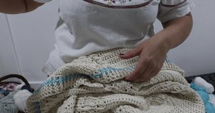 Senior adult female hands checking a just finished crochet blanket in beige cotton yarn, interlocking braids, blue detail, original embossed crochet stitch pattern. Handmade craft creativity