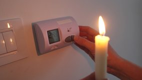 Energy crisis. Woman's hand in complete darkness holding a candle to investigate thermostat during a power outage. Blackout concept.