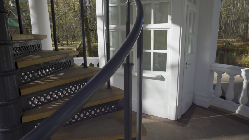 Vintage spiral staircase in an elegant white gazebo. Metal stairs up with wooden steps in a park in Kemeri. Background in the arches of autumn trees on a sunny day. Latvia