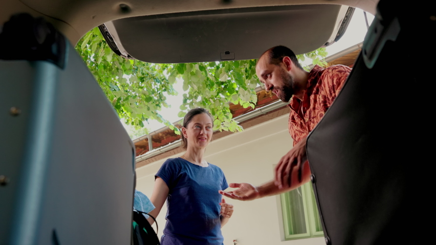 Casual family packing voyage luggage and trolleys inside car trunk while getting ready for summer vacation. Tourists putting baggage inside vehicle while going on holiday citybreak together.