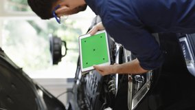Vertical Video of Car Service Mechanic Uses Tablet Computer with Green Screen Mock Up Chroma Key that is Pointed at an Enginer Bay. Specialist Inspecting the Vehicle in Order to Find Broken Components