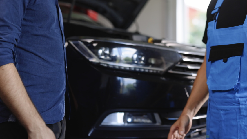 Mechanic and customer shaking hands in an auto repair shop, car service. Two unrecognizable men auto mechanic and client shaking hands at the background of vehicles. Car business, repair services. Royalty-Free Stock Footage #1093108057