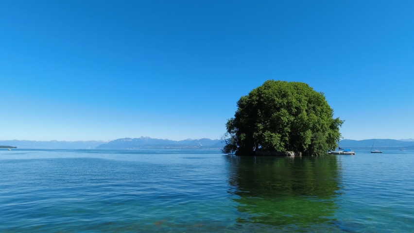 Island with lush green trees on lake Geneva between Switzerland and France. Clear green lake with island in the middle