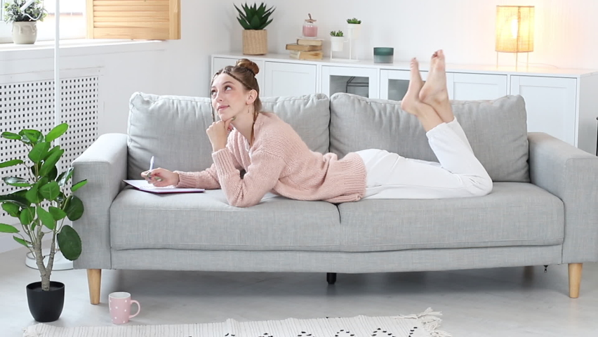 smiling woman and writes in a notebook on the sofa lies at home. lazy morning