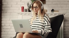 Dreamy attractive woman sitting on a chair in modern living room and talking on laptop by video chat. Study, learning, remote work, freelance.
