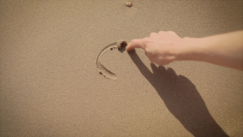 Close up view of woman hand drawing heart with finger on sand at beach. Freedom lifestyle and traveling in holiday concept