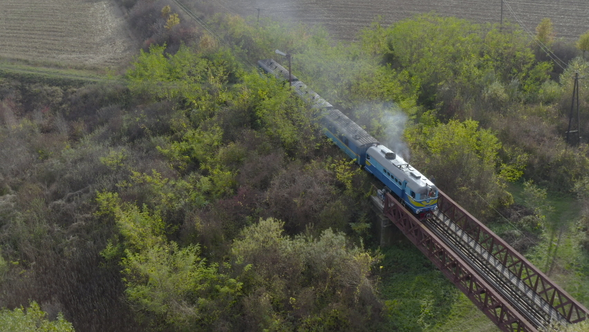 Aerial view of a train traveling over a railway bridge over a river. Drone flight over the locomotive and carriages of the narrow gauge railway.