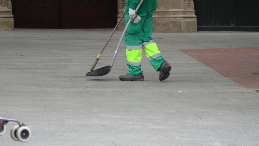 A city cleaning worker in a green uniform is sweeping the city pavement with a broom. | Shutterstock HD Video #1093121471