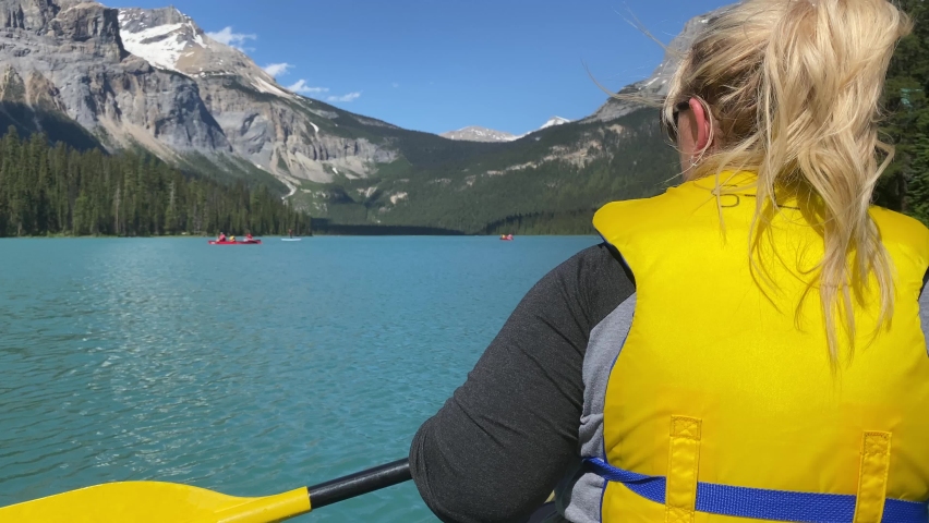 Blonde woman paddles a canoe on Emerald Lake in Canada