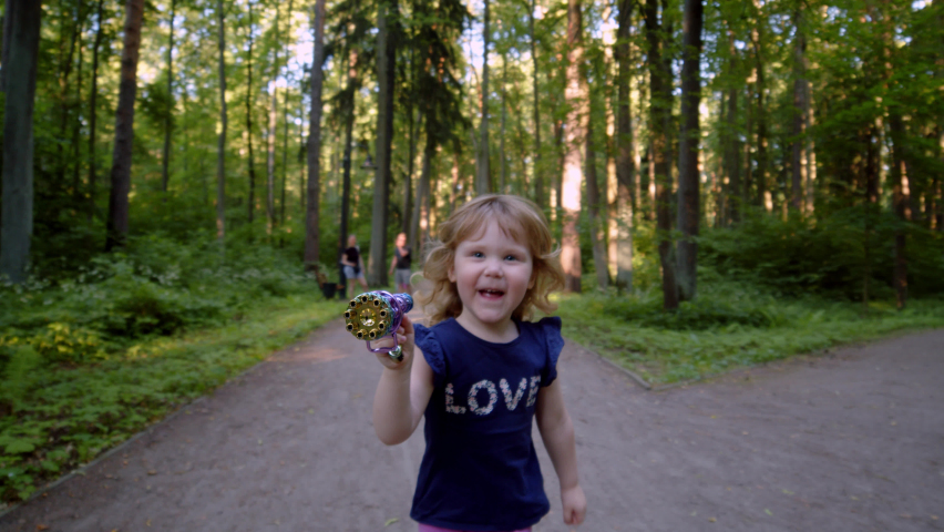 happy kid blows bubbles from special manual bubble machine outdoors in park. child rejoices at multi-colored bubbles, which turn out to be small. Great family relaxation in park with little daughter.