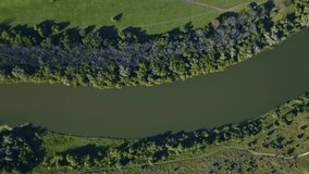 Aerial video drone footage of a large river surrounded by green fields. Top view. Meadow, paths and green trees. 
