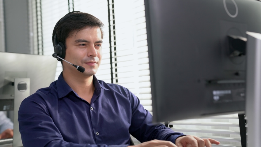Young competent asian male call center agent working at his computer while simultaneously speaking with customers. Concept of an operator, customer service agent working in the office with headset. | Shutterstock HD Video #1093132963