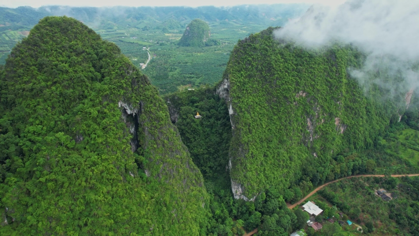 Aerial view over the temple (Tham Nam Lod Cave Temple) Beautiful Buddha statue on the hill. Chumphon province, Thailand. clouds and mountains in the morning. drone. 4k
