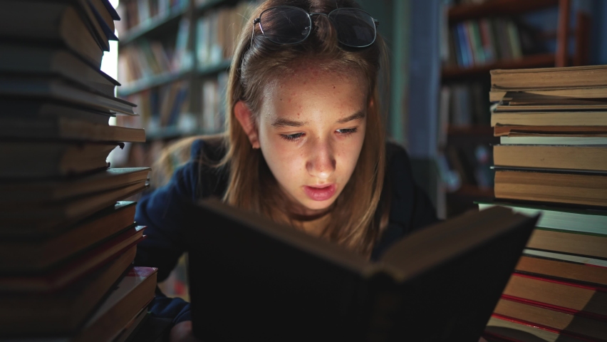 Girl is sitting in library between the bookshelves and reading book aloud for finding information. Spend time in literature storage to gain new knowledge. Interesting work from school literature. | Shutterstock HD Video #1093135081