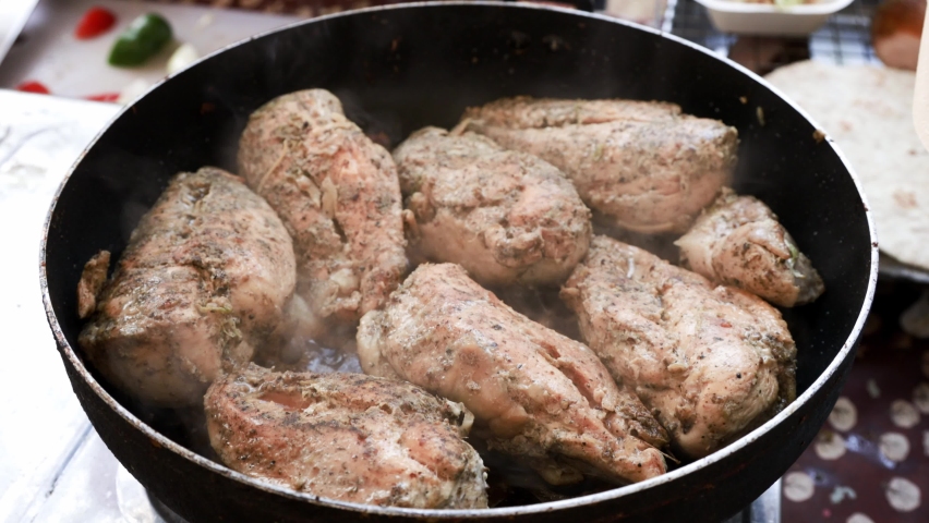 Cooking chicken taco series: Food vendor grilling chicken breasts in a hot frying pan in preparation to make taco at the food stall.