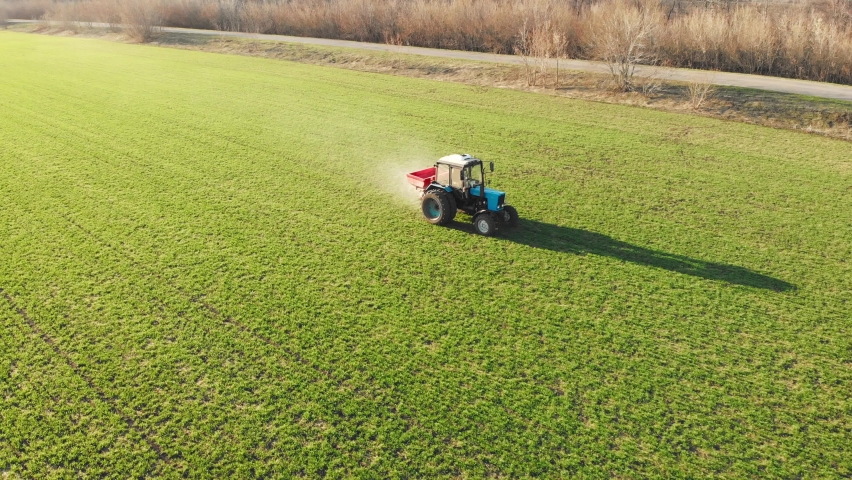 Drone footage tractor spreading artificial fertilizers in green field. Farming tractor spraying on field with herbicides. Industrial machine fertilizing a field.Chemicals used by agricultural tractor. | Shutterstock HD Video #1093142177