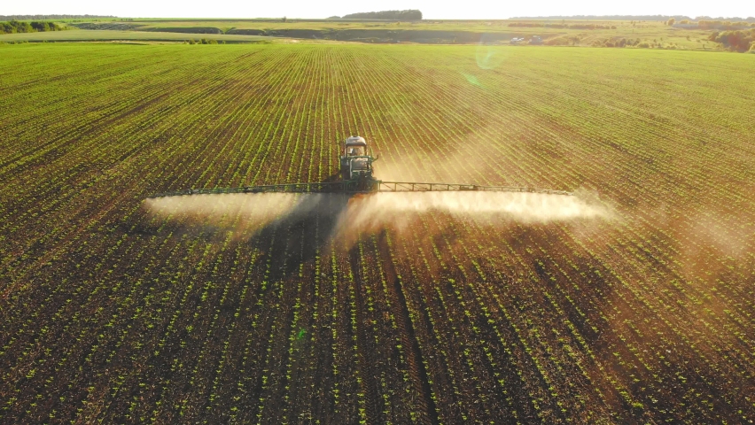 Aerial footage. Pesticide Sprayer Tractor working on a large green field at sunset. Aerial shot following on the side a tractor spraying wheat field against diseases. Farmer spraying soybean fields. | Shutterstock HD Video #1093142179