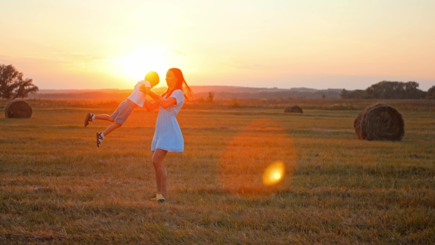 Young mother is holding hands and spinning her little son on picturesque field in sunset or sunrise. Happy family in nature in countryside in summertime. Joyful moments of childhood and motherhood. | Shutterstock HD Video #1093142191