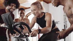 Diverse group of fit young adults supporting Caucasian female friend while she cycles on stationary exercise bike at an indoor fitness gym. - Powered by Shutterstock - Get 15% off with code: PIKWIZARD15