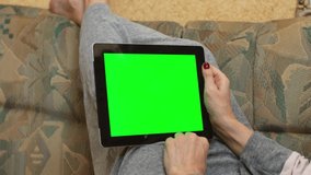 An adult woman lies on a sofa and looks at a tablet. Green screen.