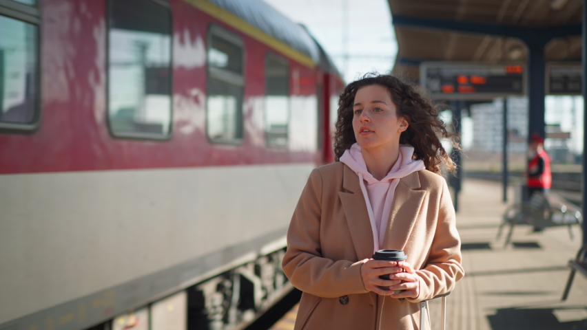 Portrait of happy young traveler woman with coffe and luggage at train station platform