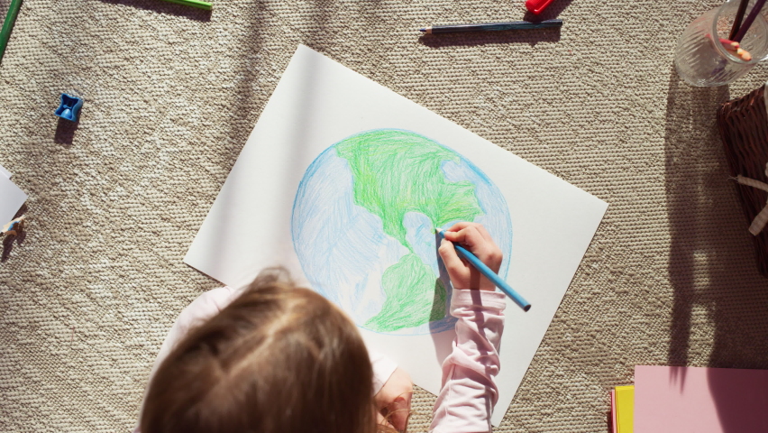 Top View: Little Girl Drawing Our Beautiful Green Planet Earth. Child Having Fun at Home on the Floor, Imagining Our Planet as a Happy Place with Clean, Sustainable Living. Cozy Sunny Day. Zoom out Royalty-Free Stock Footage #1093149755