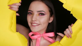 A beautiful young girl model with a bright juicy yellow fashion make-up and a pink bow around her neck on a background of stylish yellow paper. Fashion model image