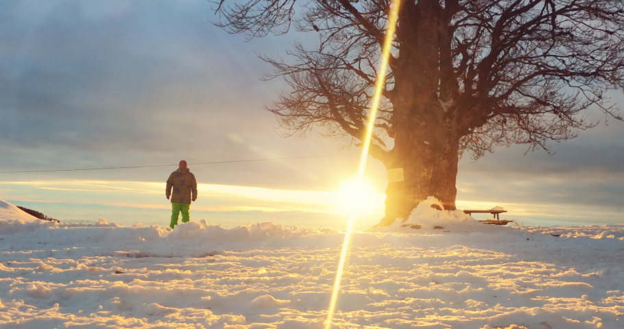 Successful hiker who conquered the top of mountain standing on a cliffs edge in the deep powder snow with raised hand and enjoying the sunset, sunrise
