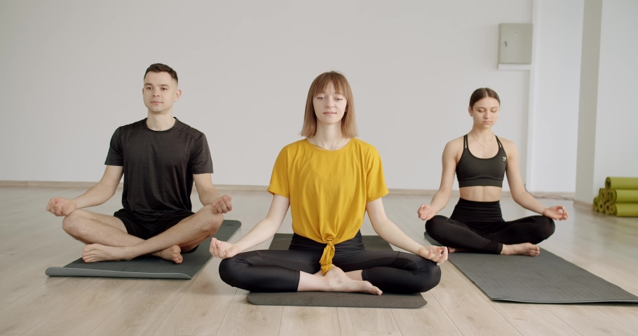Enjoying healthy lifestyle exercise in fitness studio, lotus pose work out, Yoga class meditating together indoors, concentration exercise. relaxing after group exercises in class room. Yoga Club Royalty-Free Stock Footage #1093156079