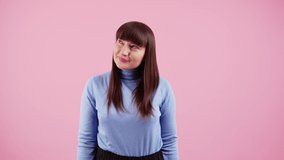 White woman with dark long hair and fringe looking from side to side and then at camera choosing between two options uncertain. Pink background. High quality 4k footage