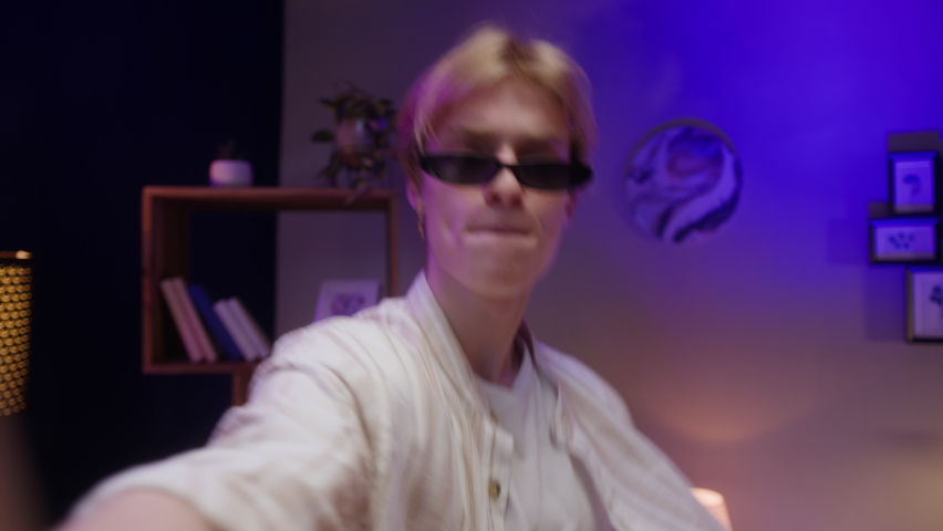 Man recording dance video on phone camera in living room. Young male student or teenager dancing at home for musical clip. Blogger making music content for channel.