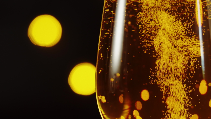 Foamy beer in glass close-up. Alcohol golden beer drink in mug. Fresh pale ale on black background with lights, celebration, holiday. 