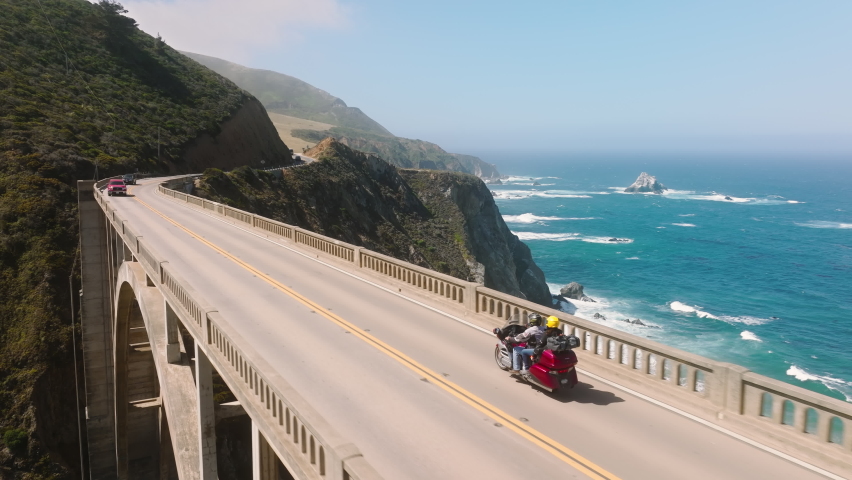 Couple riding on vintage motorcycle by beautiful Big Sur coast with cinematic landscape. Extreme vacation concept, motorbikers on motorcycle rides scenic mountain road. Freedom, life enjoyment