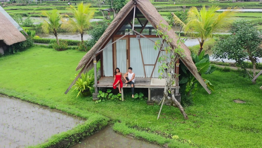 young couple sitting on balcony of rice field hut in Ubud Bali, aerial